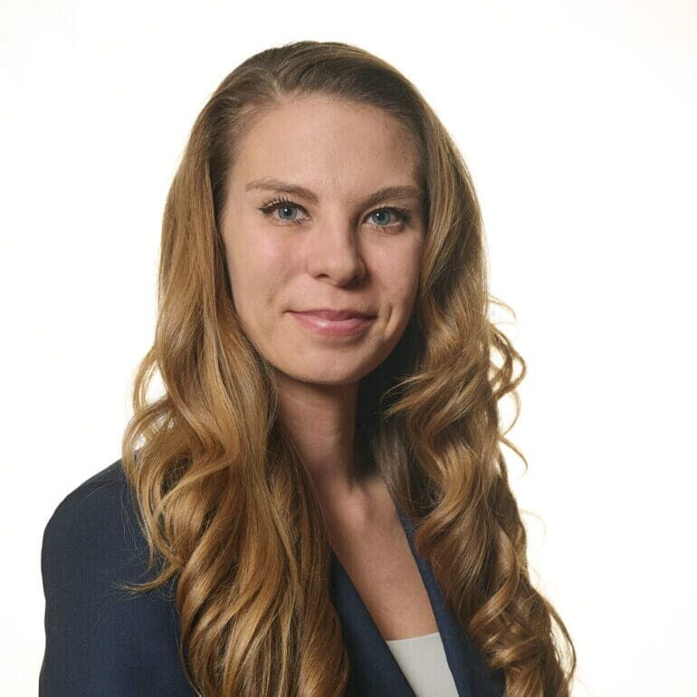 Headshot of Sarah Haney, a senior consultltant at Bizcom. She is wearing a blue suite coat partially covered by her long hair.